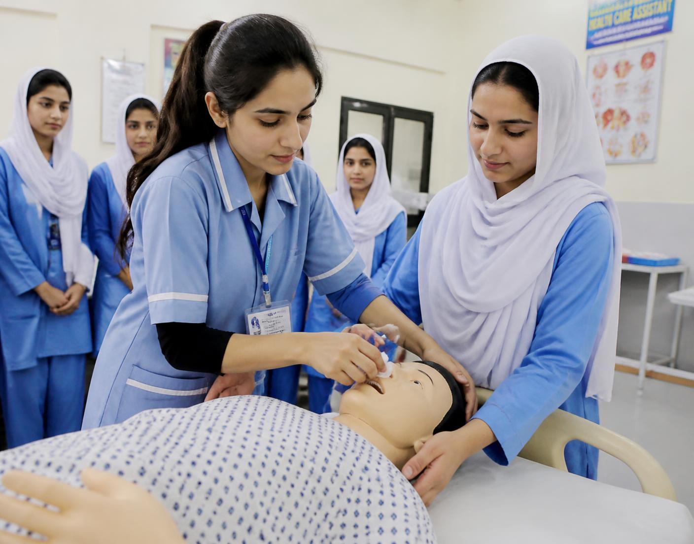Trainee healthcare assistants practising patient care with a training mannequin